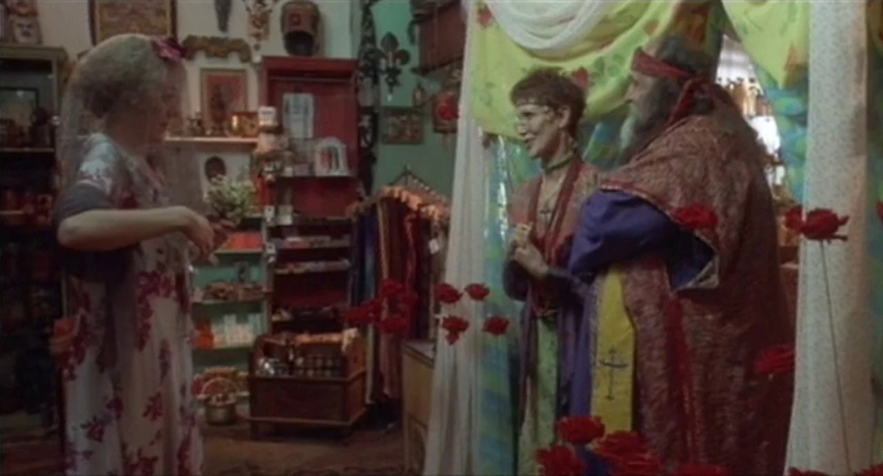 The Annihilation of Fish (1999) movie still: medium — A cluttered shop interior filled with shelves, hanging fabrics, and religious icons. One woman…