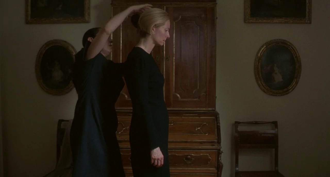 Making of: I Am Love (2009) movie still: medium — A dimly lit room features a wooden cabinet and framed paintings on the wall. A woman in a black…