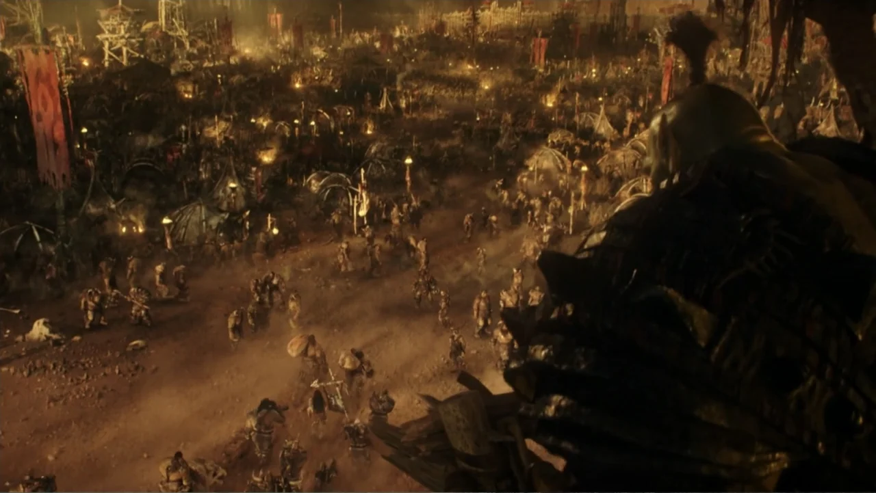 Warcraft (2016) movie still: wide — A vast, dusty fantasy encampment is filled with numerous tents and scattered groups. An armored orc stands in…