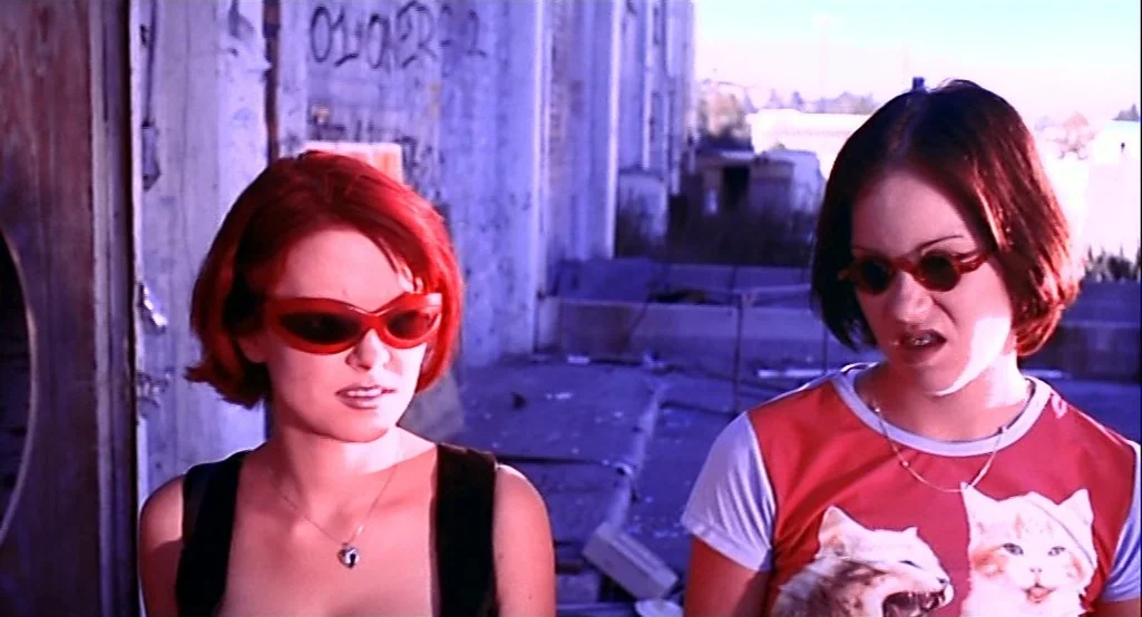 Nowhere (1997) movie still: medium — An abandoned concrete structure features graffiti-covered walls and rubble on the ground floor. Two young women…