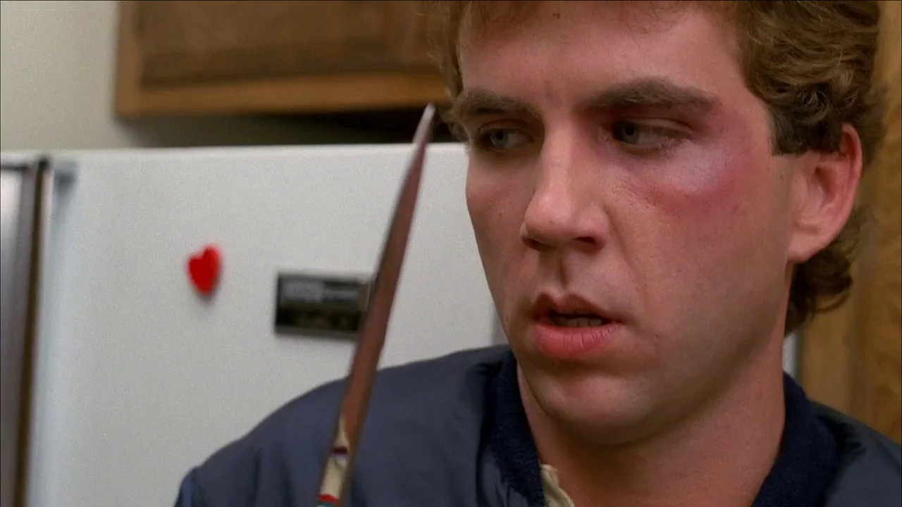 The Slumber Party Massacre (1982) movie still: closeup — A man stands in front of a white refrigerator with a red heart magnet. He looks at a thin…