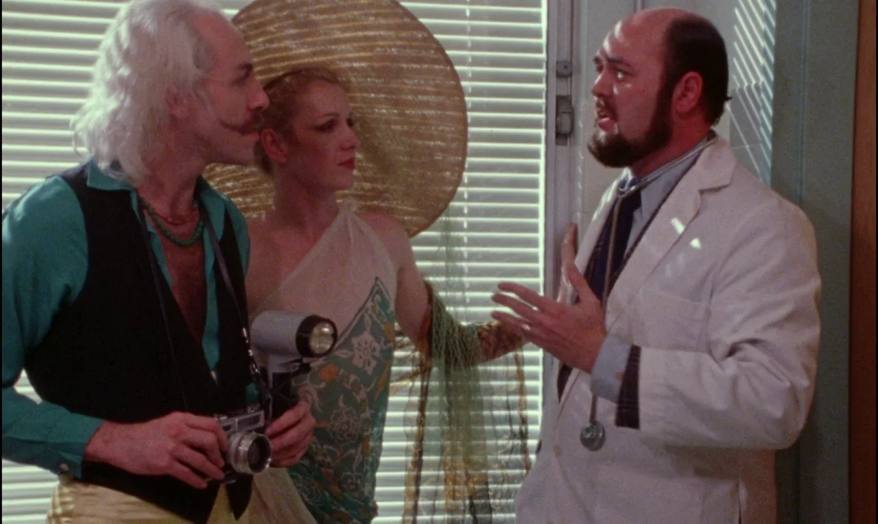 Female Trouble (1974) movie still: medium — An interior office space with horizontal window blinds filling the background. A doctor in a white coat…
