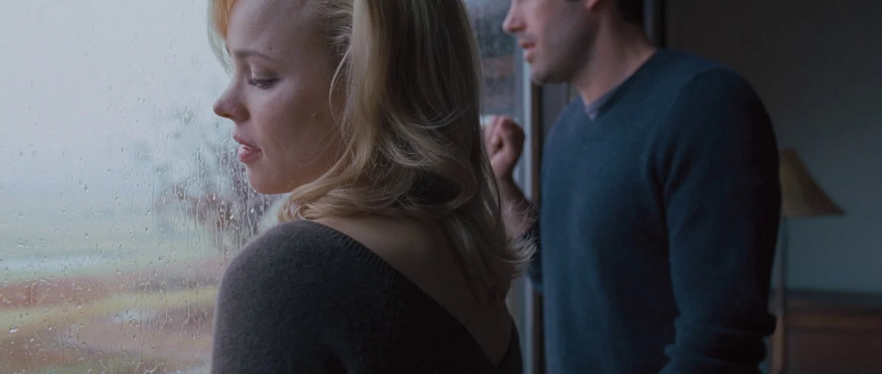 To The Wonder (2012) movie still: medium — A modern room features a large window covered in raindrops looking out onto fields. A blonde woman and a…