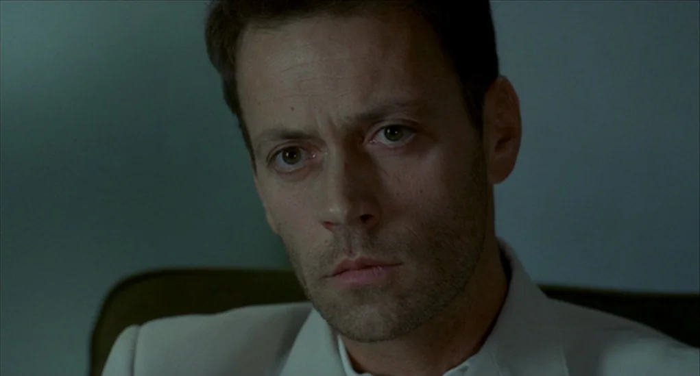 Anatomy of Hell (2004) movie still: closeup — A close-up view of a man's face against a simple, muted grey background wall. The man maintains a…