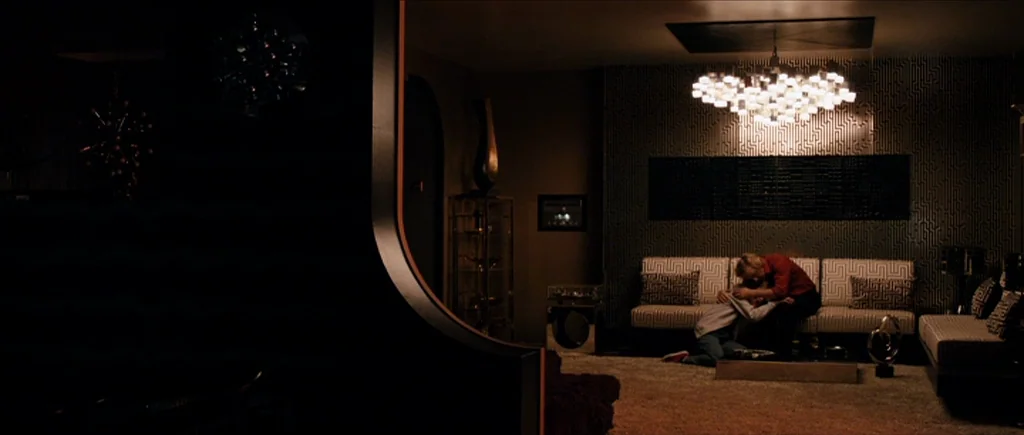 The Look of Love (2013) movie still: wide — A dark, modern interior features geometric wall patterns and a large central chandelier fixture. Two…