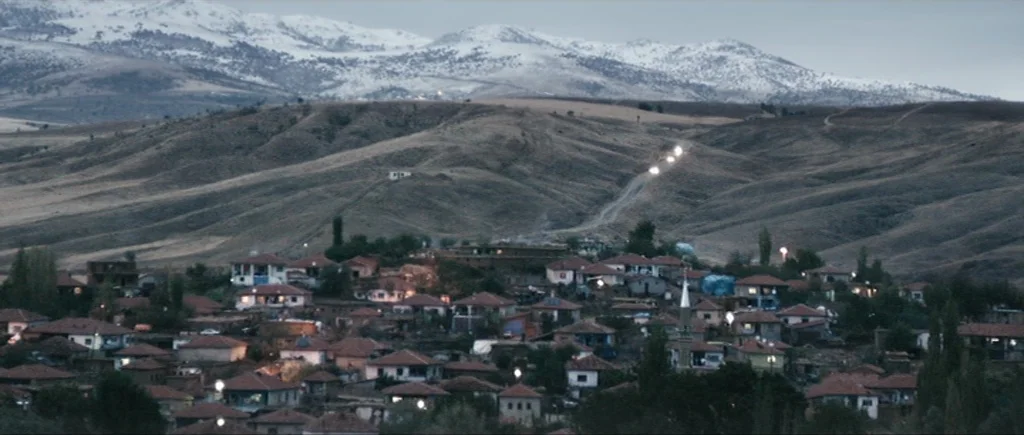 Once Upon a Time in Anatolia (2011) movie still: establishing — A rural village clusters at the base of expansive, snow-capped brown hills. Numerous…