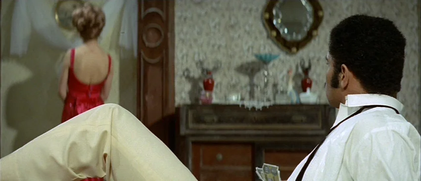 Whity (1971) movie still: medium — A dimly lit room features patterned wallpaper and an antique dark wood console table. A man with his legs up…