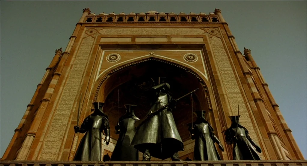 The Fall movie still: wide — Five figures in black metallic armor stand before a large, ornate stone archway. The group holds weapons while…