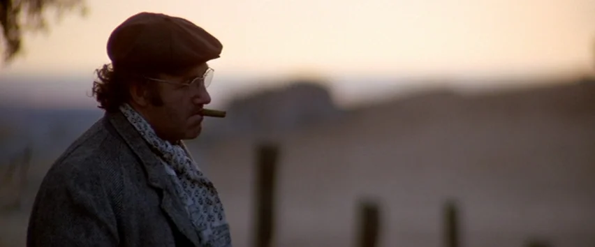 Scarecrow (1973) movie still: medium — An open rural field is depicted at dusk with a soft horizon in view. A man in a tweed coat and flat cap…