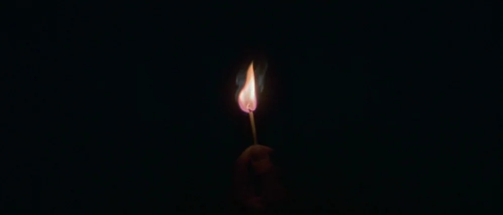 The People vs. Larry Flint (1996) movie still: closeup — A lone match flame burns against a completely black, undifferentiated background. The light…