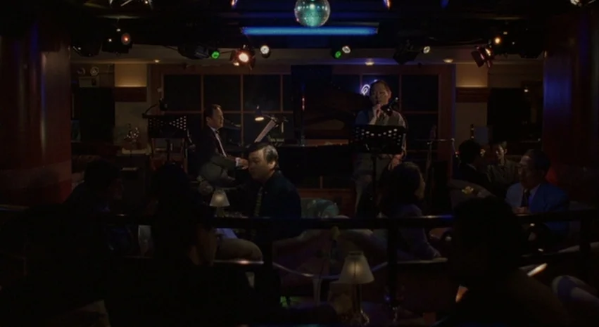Yi-Yi (A One and A Two) (2000) movie still: wide — A dimly lit lounge featuring a small stage with a performer and seated patrons. Several round…