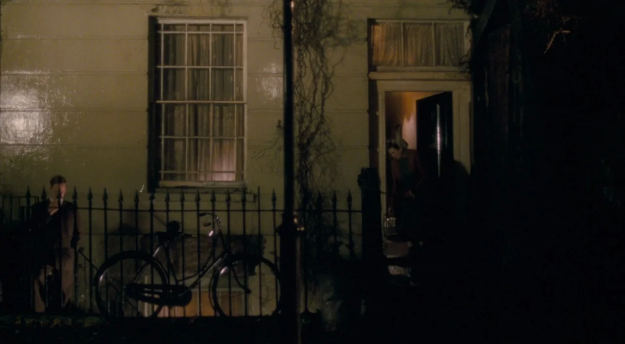 The Deep Blue Sea (2011) movie still: wide — A residential building exterior at night with a metal fence and bicycle in front. A man stands outside…