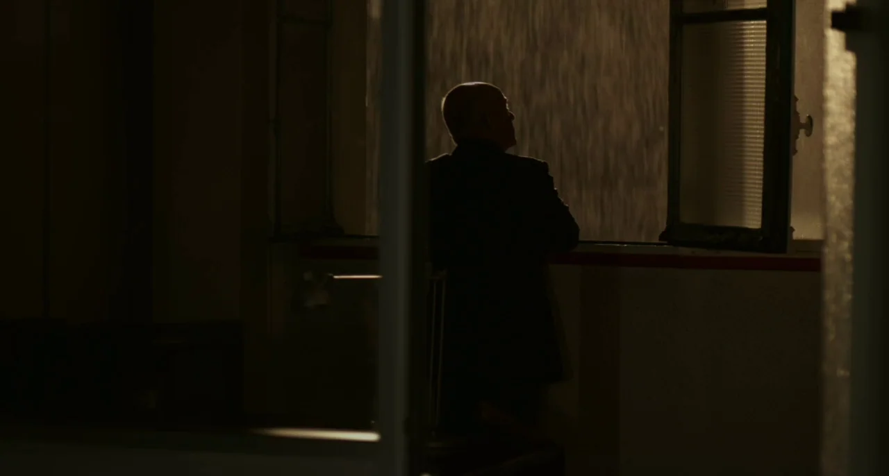 Bastards (2013) movie still: medium — A dark office at night with an open window looking out at rain. A man in a dark suit stands facing the window,…