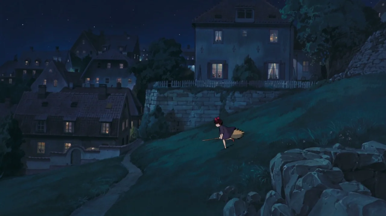 Kiki’s Delivery Service (1989) movie still: wide — A dark European-style hillside village overlooks a grassy slope under a starry night sky. A small…