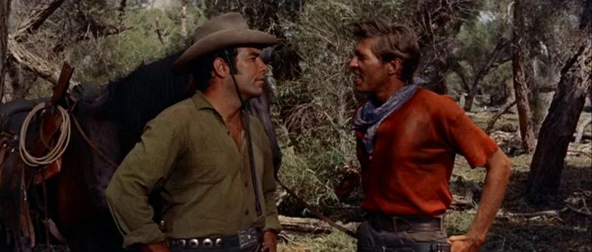 Ride Lonesome (1959) movie still: medium — Two men stand near a horse in a dense thicket of trees and shrubs. The men are engaged in conversation…