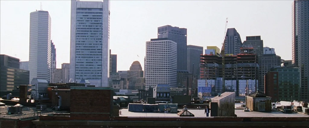 The Departed (2006) movie still: establishing — A dense urban skyline features numerous skyscrapers and a partially constructed building with…