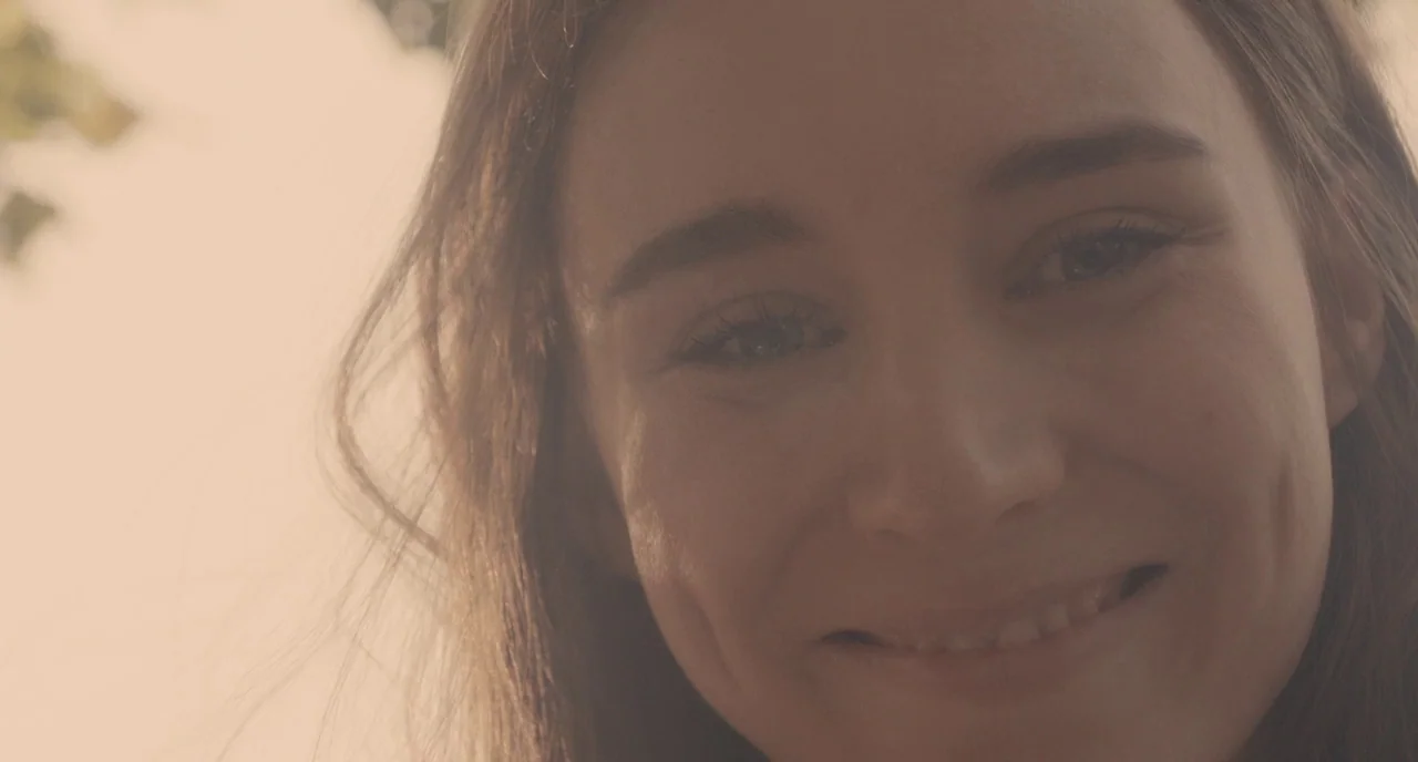 Her (2013) movie still: closeup — A close up shot of a woman outdoors during golden hour. The subject is looking towards the camera with a smile.