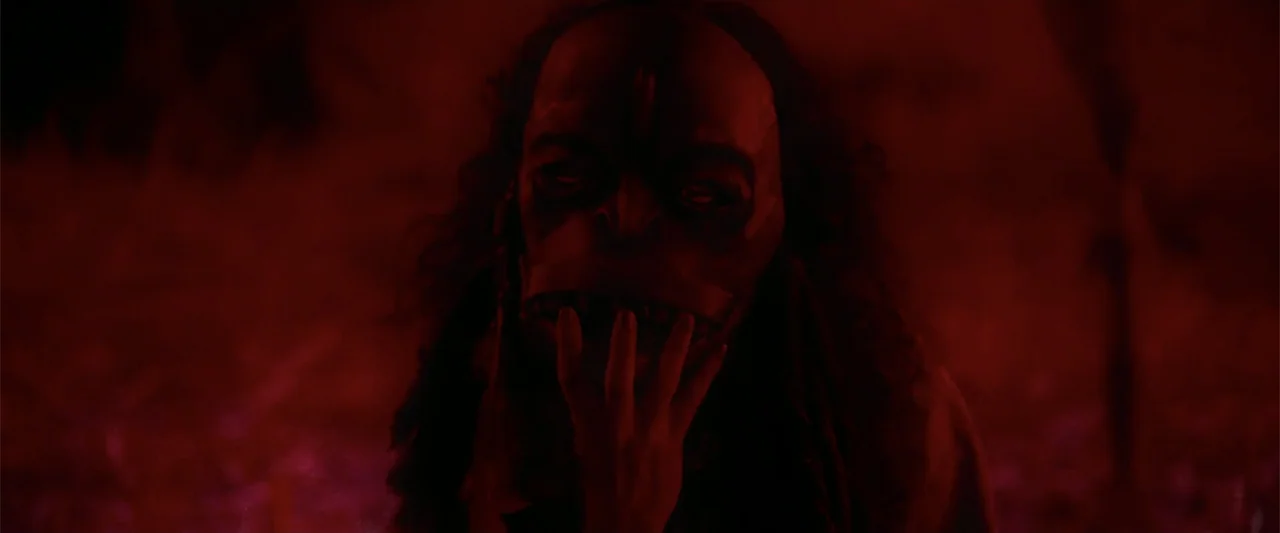 Evil Eye (2020) movie still: closeup — A dark outdoor space is completely bathed in intense, unnatural red illumination. A single figure stands…