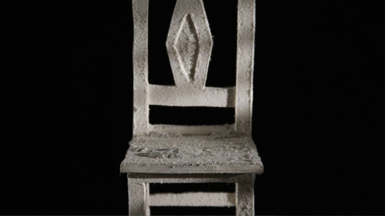 Bestia (2017) movie still: closeup — A miniature wooden chair covered in a thin layer of white dust. The object sits perfectly centered against a…