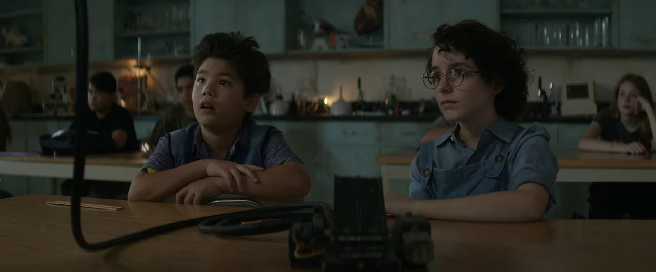 Ghostbusters: Afterlife (2021) movie still: medium — A science classroom filled with laboratory glassware and shelves. Two students sit at a desk…
