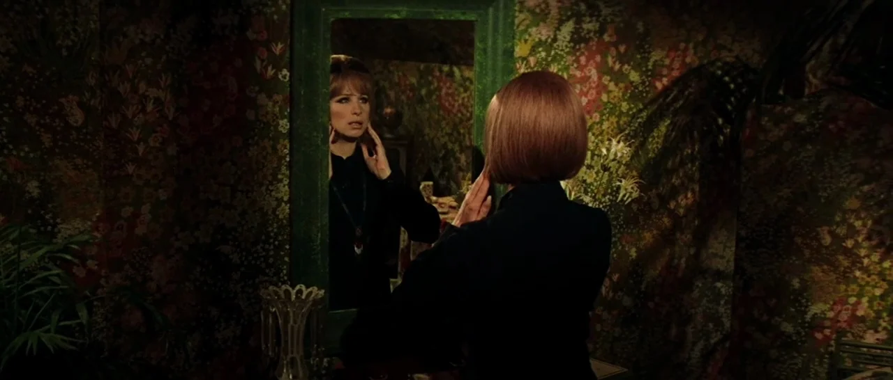 On A Clear Day You Can See Forever (1970) movie still: medium — A dimly lit room features floral wallpaper and a large rectangular mirror mounted…