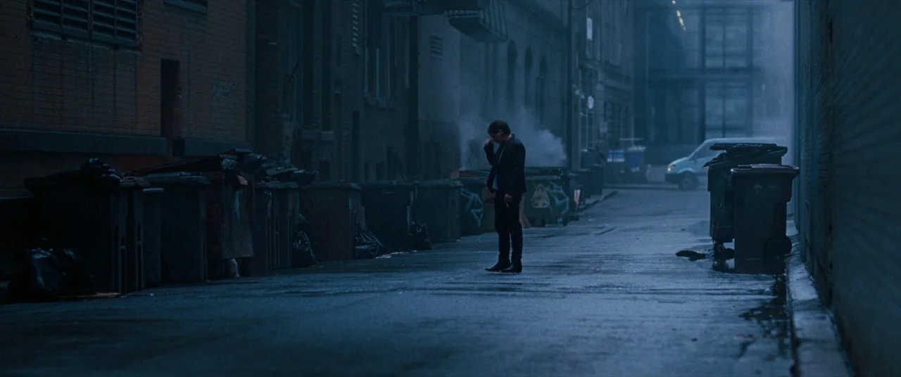 The Death and Life of John F. Donovan (2018) movie still: wide — A dark, wet city street is lined with industrial plastic trash bins and brick…