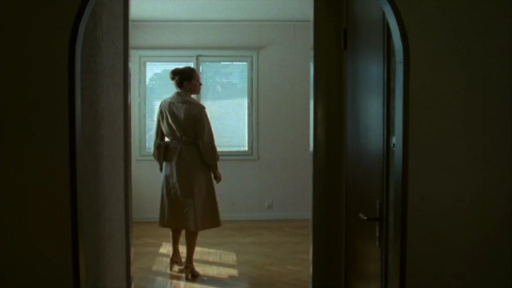 Face to Face (1976) movie still: fullbody — An empty room with light-colored walls and polished wooden floors faces a large window. A woman wearing…