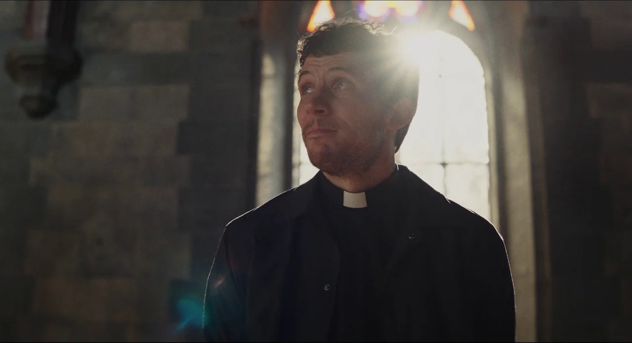 Wake Up Dead Man (2025) movie still: medium — An old stone cathedral interior features a high arched window with stained glass details. A man in…