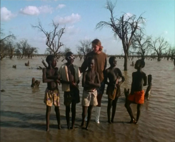 Fata Morgana (1971) movie still: fullbody — A group of children and a woman stand together in a shallow, flooded landscape. Dead, leafless trees…