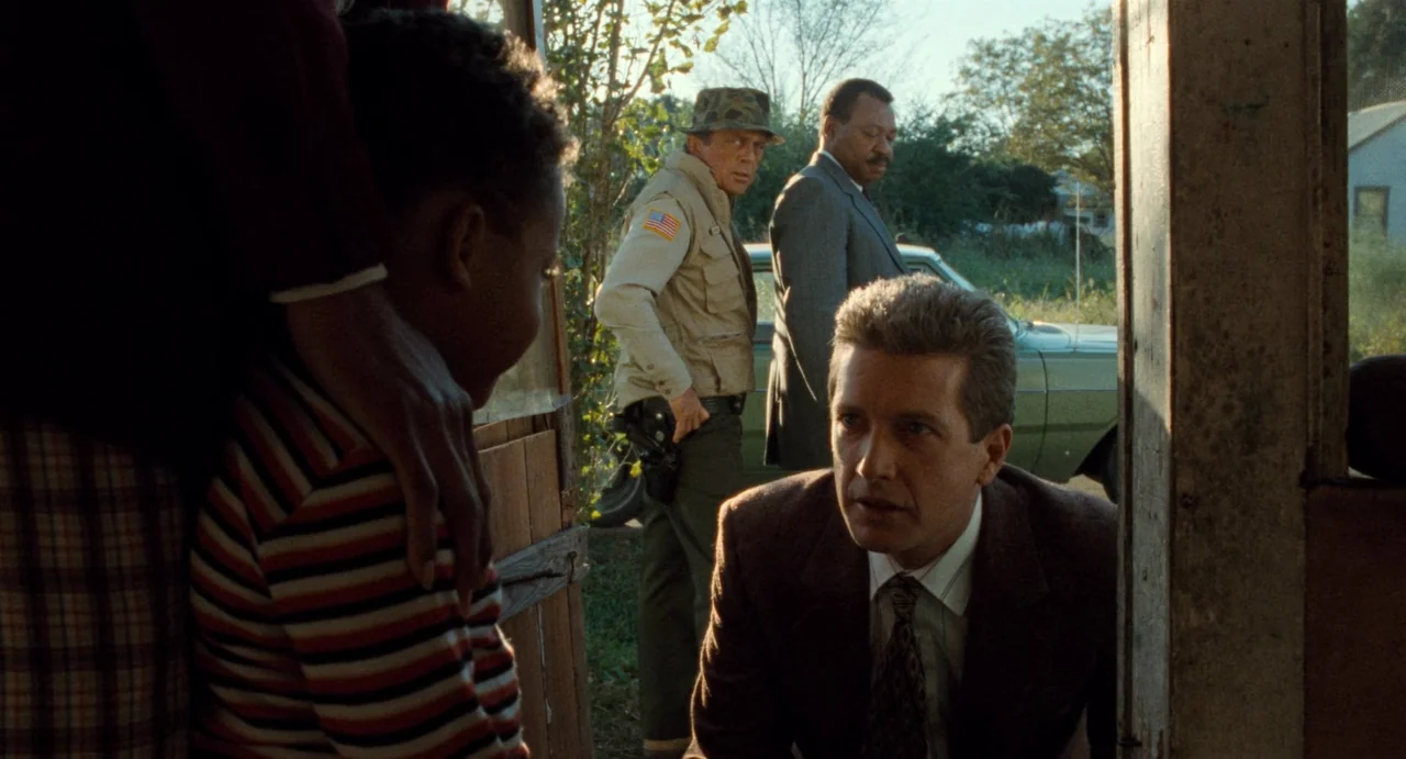 One False Move (1991) movie still: medium — A rural porch area with weathered wood framing and a glimpse of a car. Three men and a child interact…