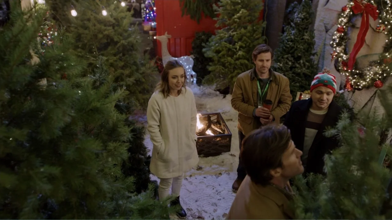 Peppermint and Postcards (2023) movie still: medium — A snowy outdoor lot filled with various sized pine trees decorated with warm lights. Four…