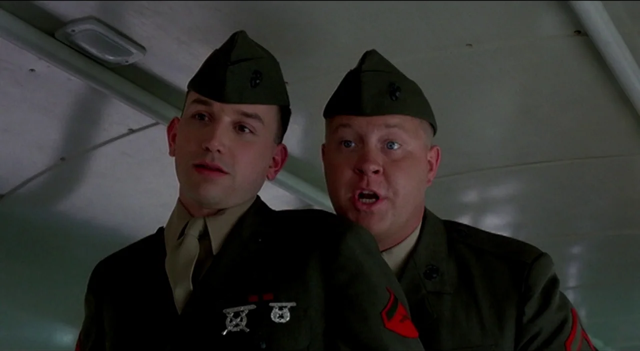 Dogfight (1991) movie still: medium — The interior of a military bus with overhead panels and smooth walls. Two young soldiers in green uniforms…