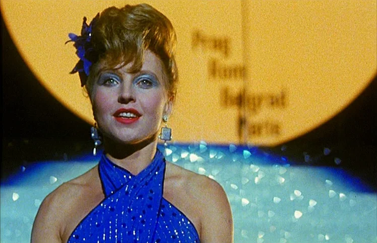 Lili Marleen (1981) movie still: medium — A woman stands on a stage in front of a massive yellow circular backdrop. She wears a sparkling blue dress…