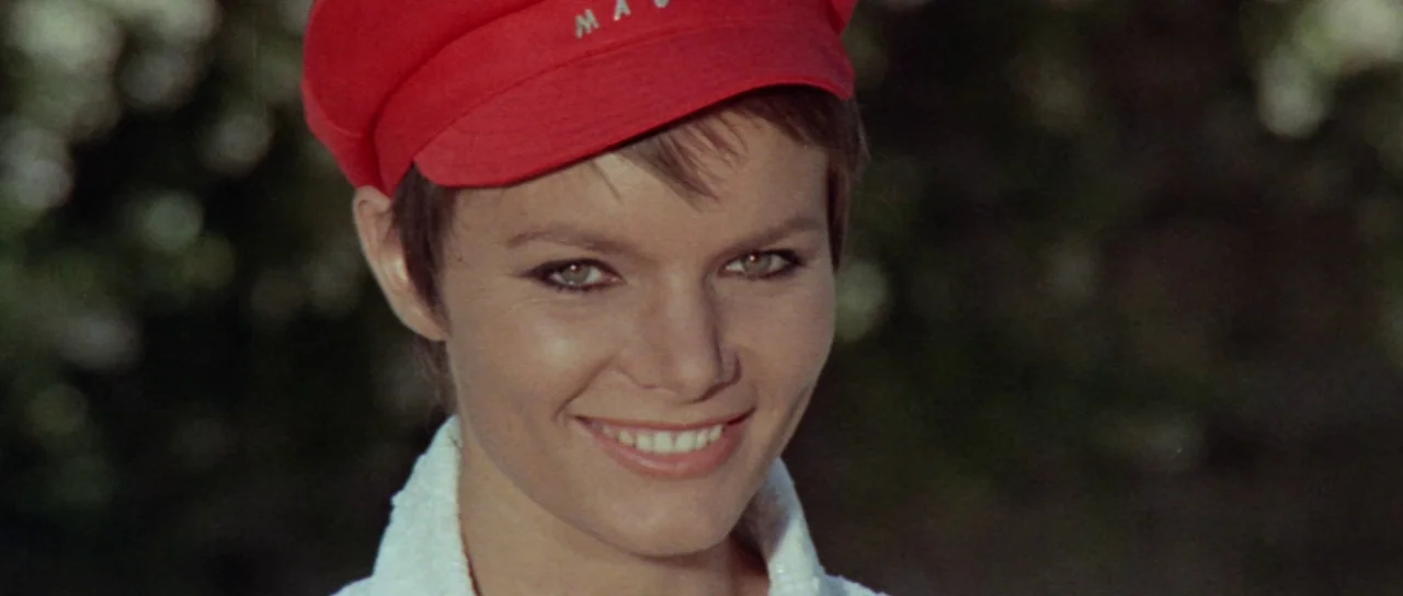 Orgasmo (1969) movie still: closeup — A woman stands outdoors with out-of-focus foliage in the background. She smiles directly at the viewer while…