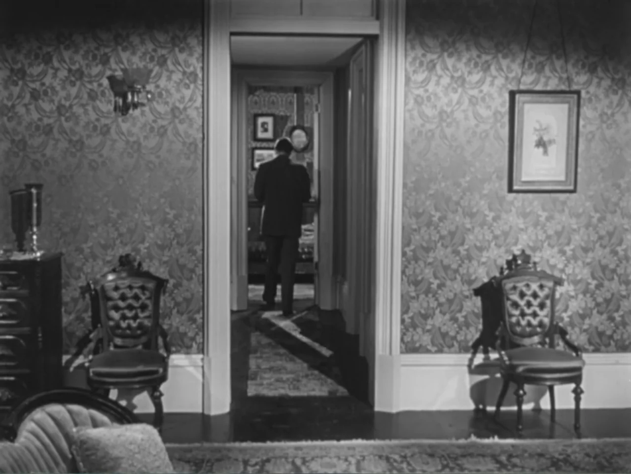 House by the River (1950) movie still: medium — A domestic interior with floral wallpaper features two matching antique chairs facing a central…