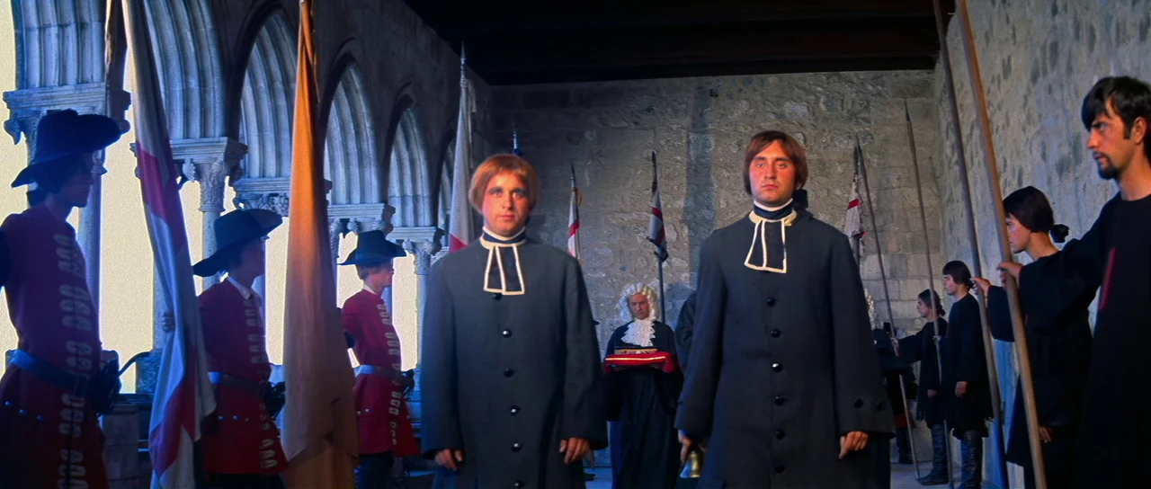 Night of the Blood Monster (1970) movie still: fullbody — A stone corridor features arched openings and flags along the left side. Two men in…