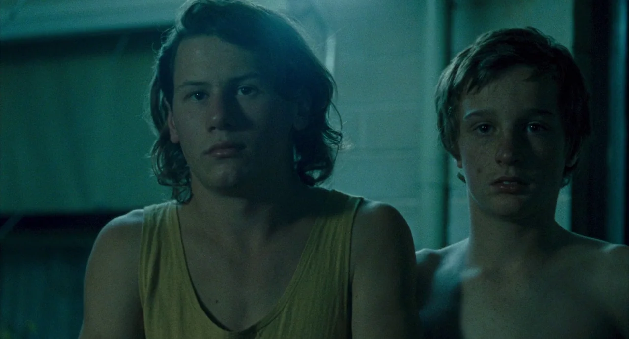 Snowtown (2011) movie still: medium — Two teenage boys stand in a dimly lit, austere interior space with concrete walls. They are facing forward,…