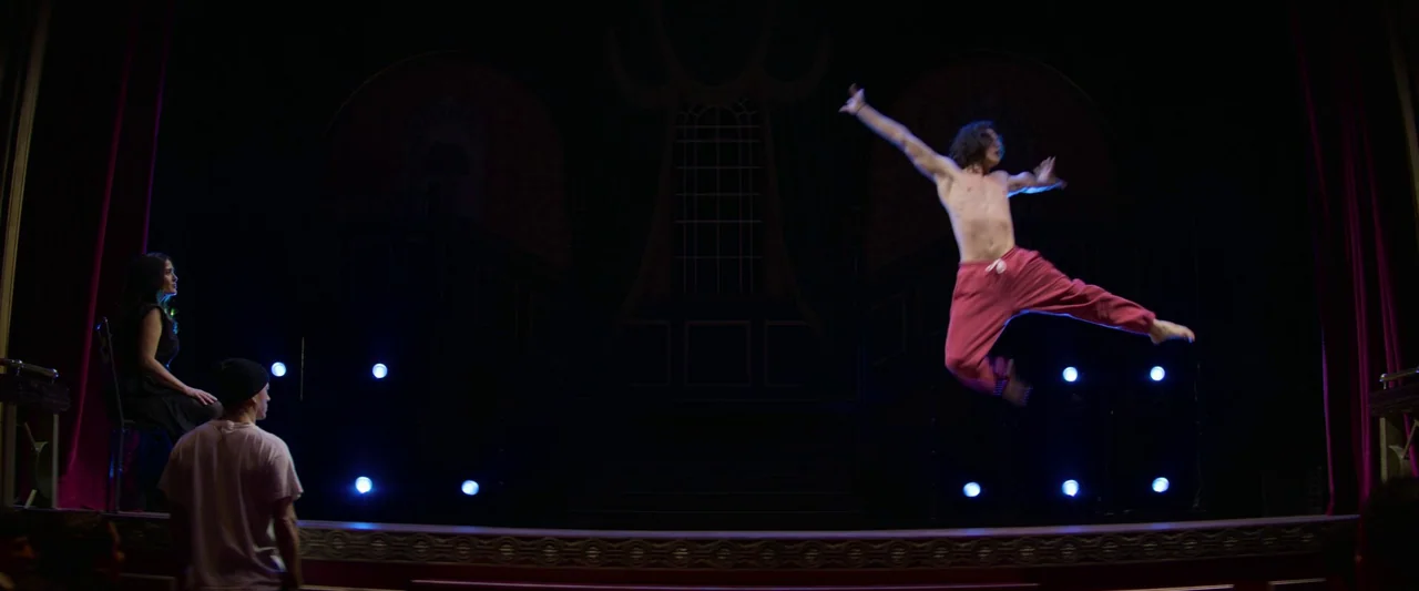 Magic Mike's Last Dance (2023) movie still: wide — A dimly lit stage interior with red velvet curtains frames the performance area. A male dancer…