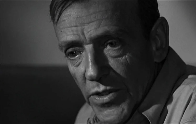 On The Beach (1959) movie still: closeup — A dimly lit, nondescript room serves as the setting for this close-up shot. A middle-aged man with…