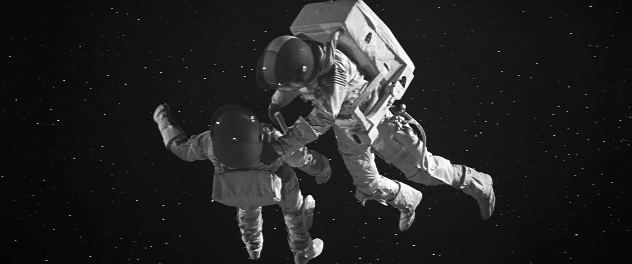Roma (2018) movie still: fullbody — Two astronauts float against a stark black background filled with tiny distant stars. One astronaut reaches out…