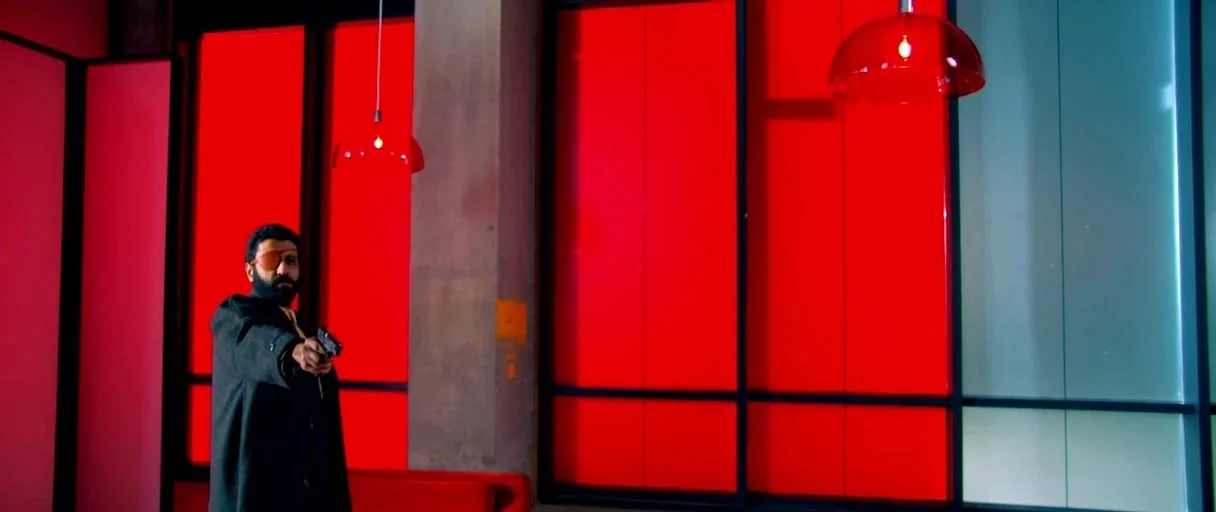 Utopia (2013) movie still: medium — An interior space features large, vertically segmented panels backlit in intense red and blue. A man with a…