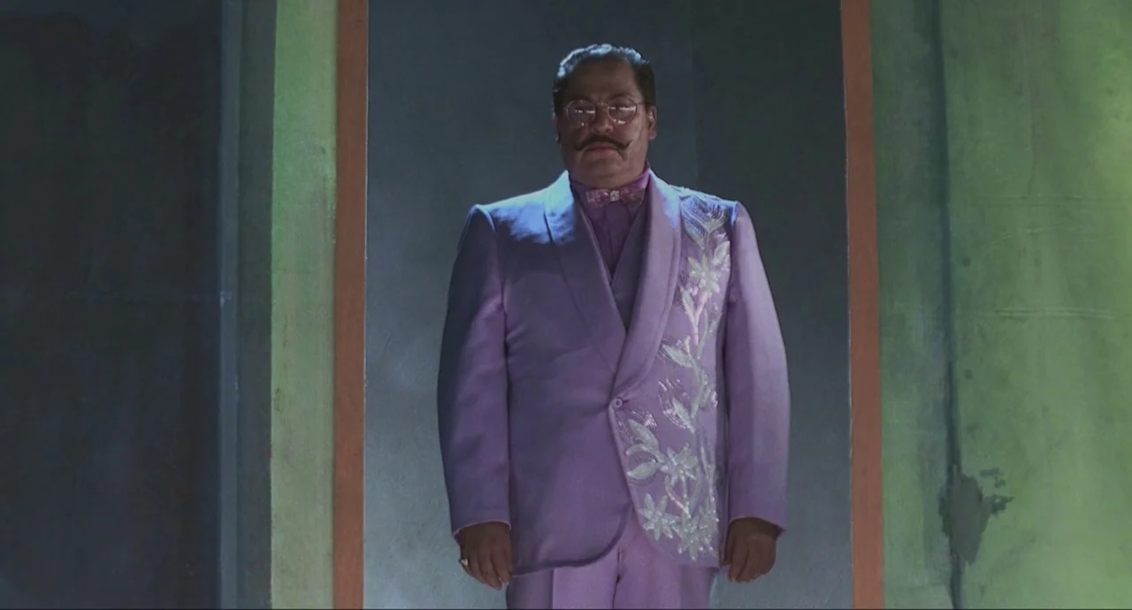 Santa Sangre (1989) movie still: medium — A man stands centered within a narrow vertical doorway framed by lime green panels. He wears an ornate…