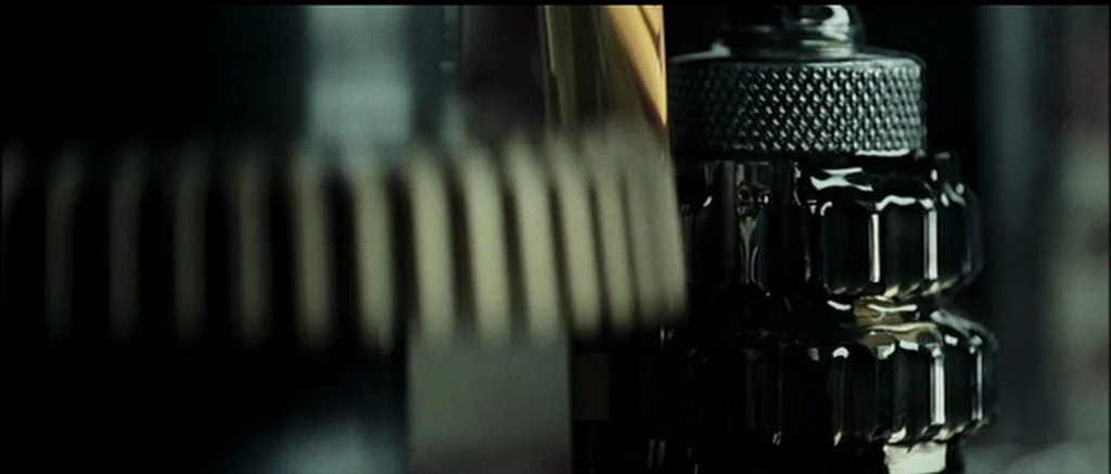 The Machinist (2004) movie still: closeup — Interlocking industrial metal gears rotate within a confined mechanical housing. Thick oil clings to the…
