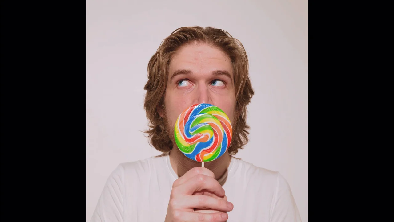 Bo Burnham: Inside (2021) movie still: closeup — A man stands centered against a plain, off-white studio backdrop. He holds a bright,…