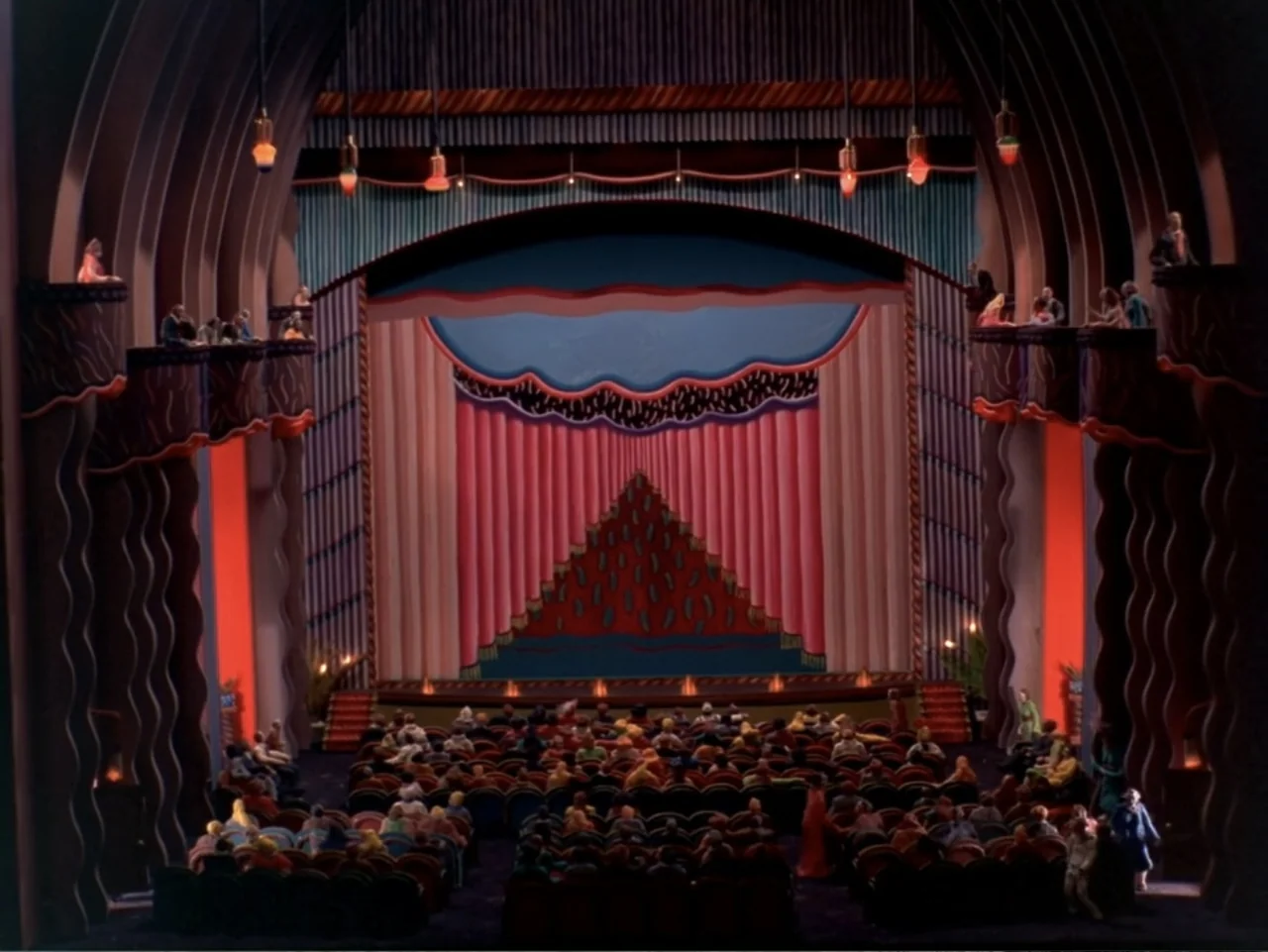 Asparagus (2007) movie still: establishing — A stylized, colorful theater interior features tiered balconies and a large, draped proscenium stage.…