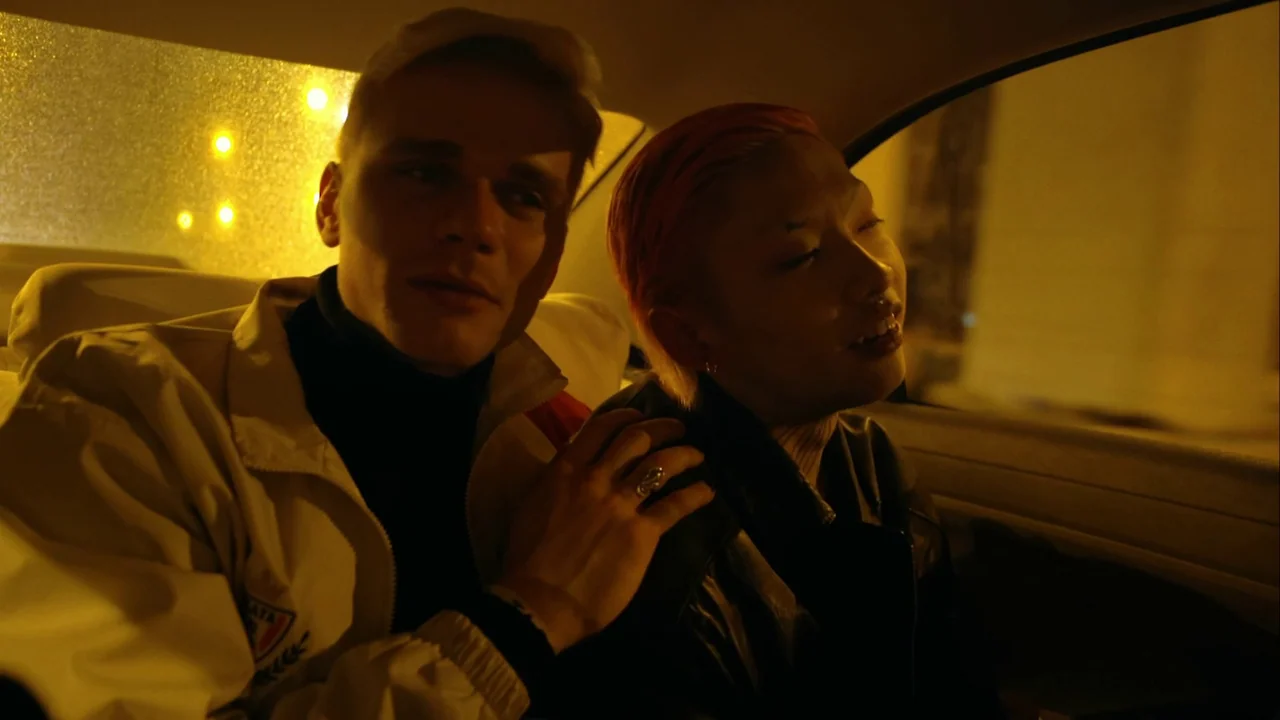 The Last Year of Darkness (2023) movie still: medium — The interior of a moving vehicle at night with yellow streetlamp glow filtering inside. A…