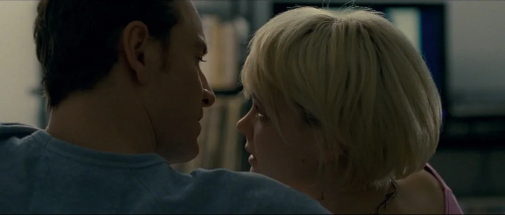 Shame (2011) movie still: closeup — A dimly lit indoor space with two people facing each other in close contact. The man is seen from behind while…