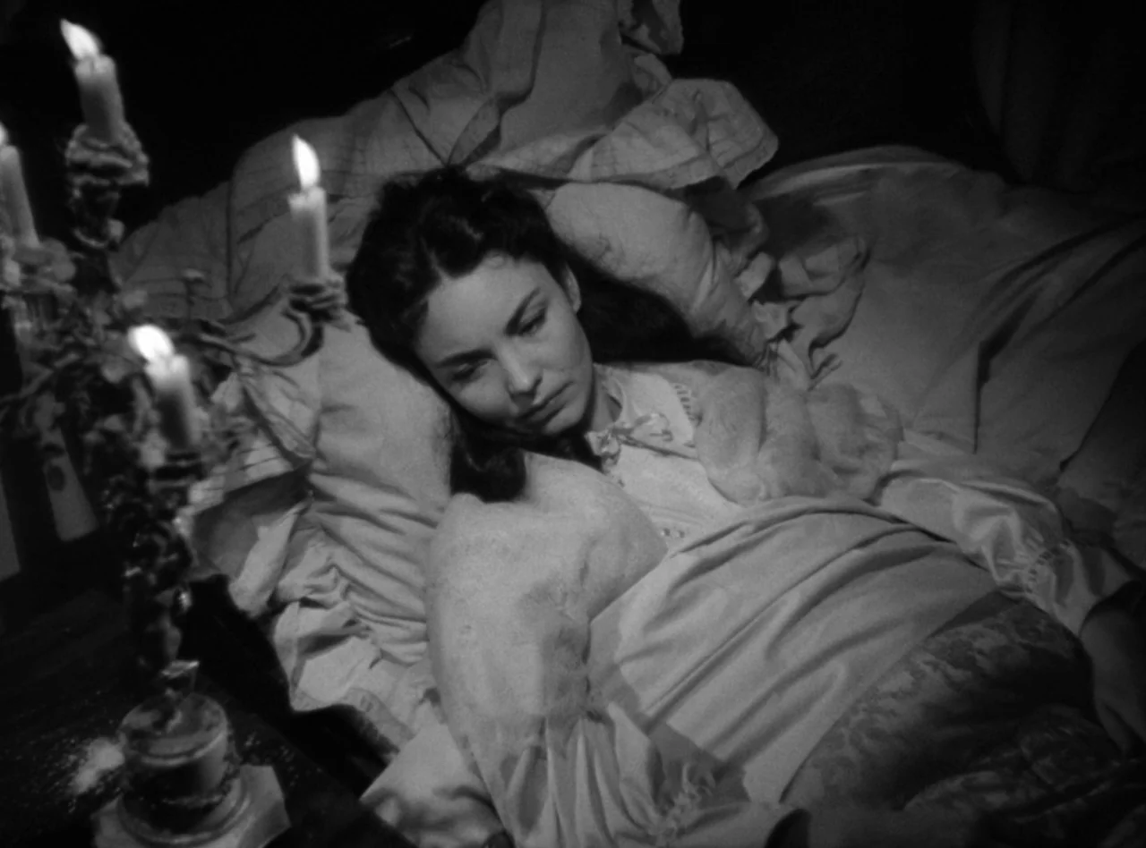 Madame Bovary (1949) movie still: medium — A woman lies in a bed draped with heavy linens in a dim room. A multi-wicked candelabra sits on a nearby…