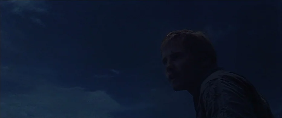 Deliverance (1972) movie still: medium — A dark night landscape featuring a sky filled with faint, wispy cloud formations. A man stands in profile,…