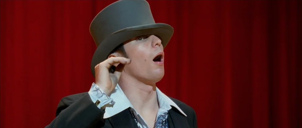 Confessions of a Dangerous Mind (2002) movie still: medium — A man in a top hat stands before a plain red curtain. He raises his hand to his ear…